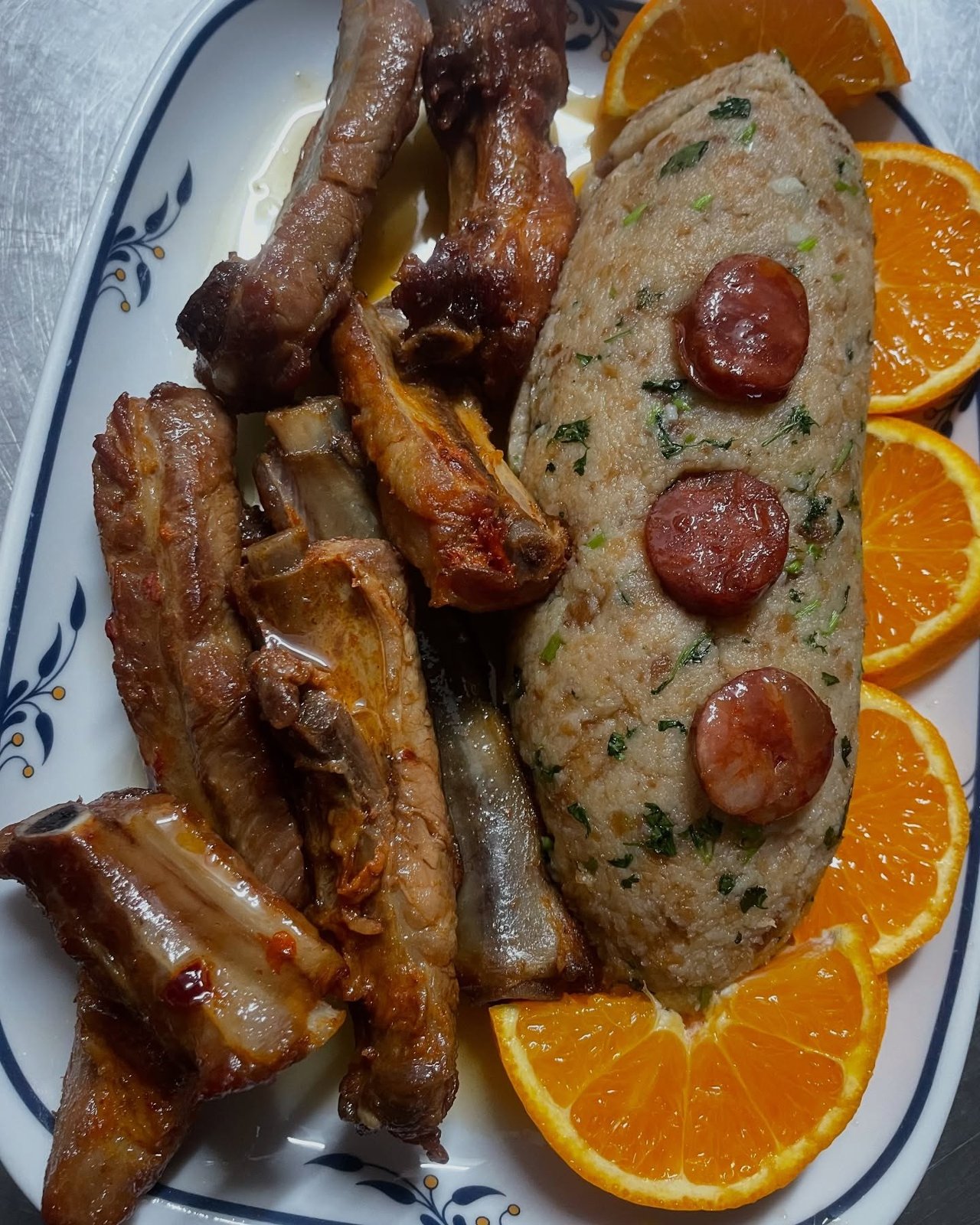 Travessa com entrecosto assado, migas com rodelas de enchido e laranja