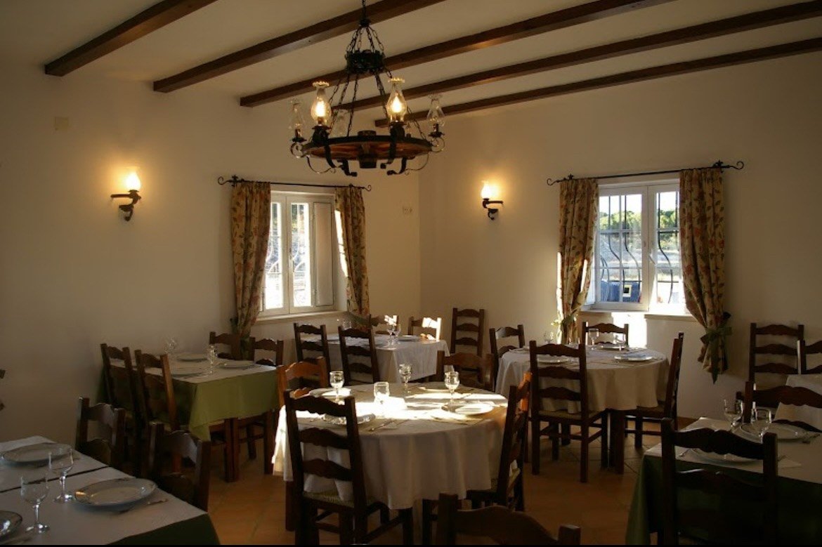 Sala de jantar com vigas de madeira, candeeiro de ferro e mesas postas com toalhas